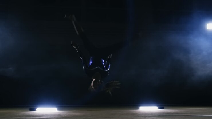 A girl performs a jump gymnastics on a dark background in the smoke in slow motion