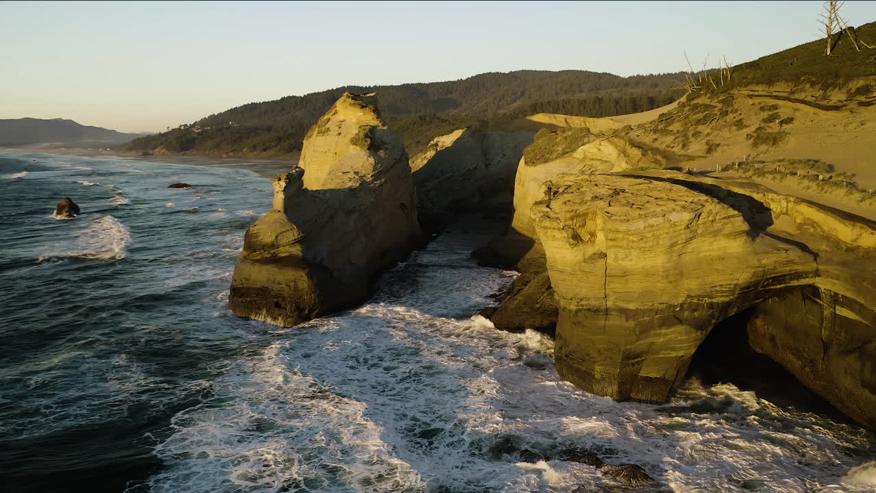 Golden light glowing on sandstone cliffs as waves crash on hidden cove, aerial
