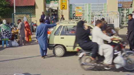 patient taxi driver parked outside a bustling islamabad marketplace filled with people shopping and socializing in pakistan.