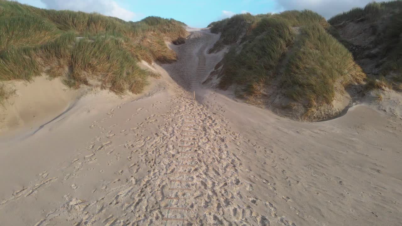 un dolly en una toma de dron captura los poderosos vientos que barren arena a través de las dunas en la playa de hvide sande, con cielos tormentosos y costa accidentada que establece la escena dramática en un día de viento en dinamarca