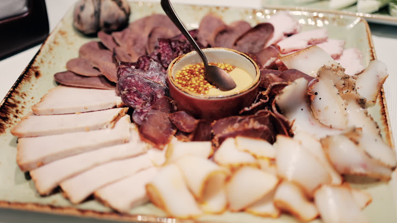 Gourmet charcuterie board with assorted cured meats, smoked slices, and a mustard seed sauce served in a bowl