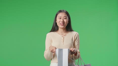 an asian shopping woman being happy after opening shopping bag while standing in front of green screen