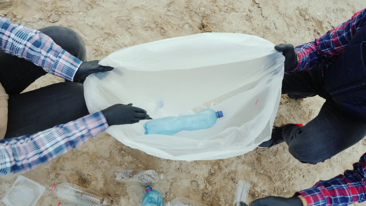 자원 봉사자들은 플라스틱 쓰레기를 가방에 넣고 환경을 돌보는 해변을 청소합니다.