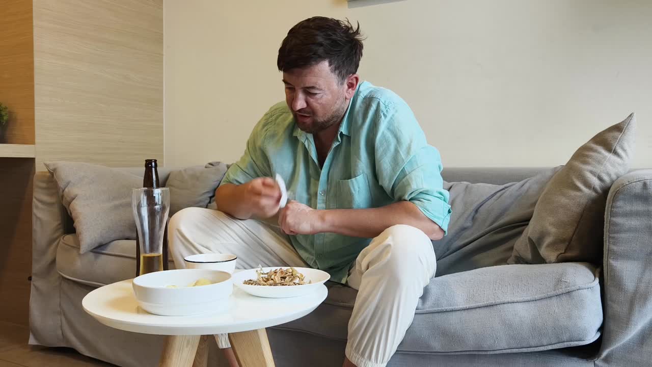 Man eating and drinking beer on a couch at home