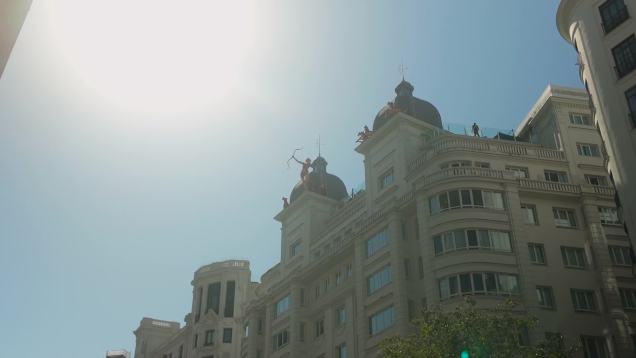 Vista en ángulo bajo de edificios y esculturas icónicos en la Gran Vía de Madrid, España. Adecuado para documentales de viajes, estilo de vida urbano y contenido de turismo europeo.