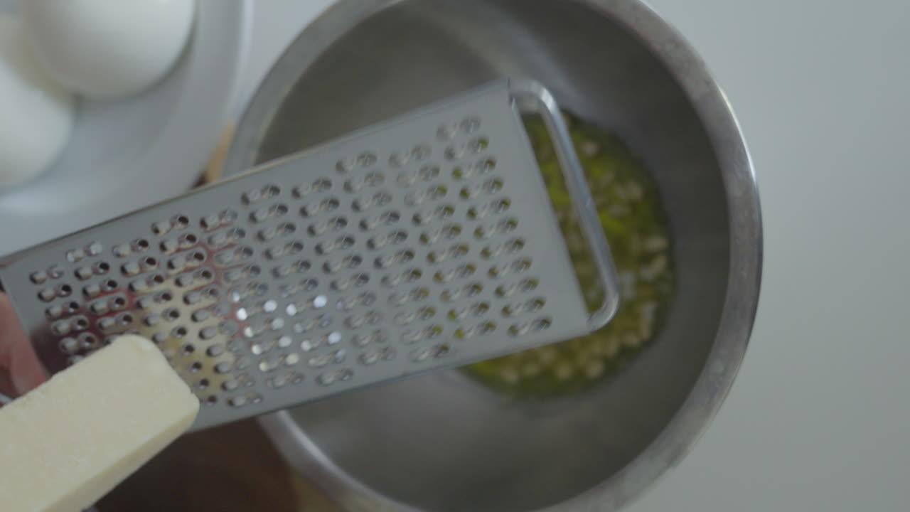 Primo piano di mani che grattugiano formaggio parmigiano italiano in una ciotola per il pesto