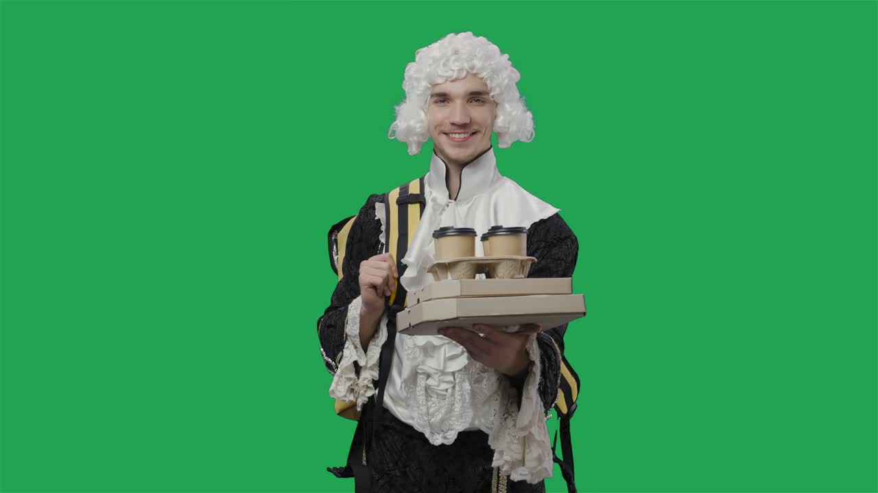 검은색 역사적인 빈티지 슈트와 색 가발을 입고 음식과 음료를 배달하는 궁정 신사의 초상화. 녹색 화면 배경으로 스튜디오에서 포즈를 취하는 젊은 남자.