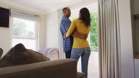 back view of biracial couple standing at window and embracing