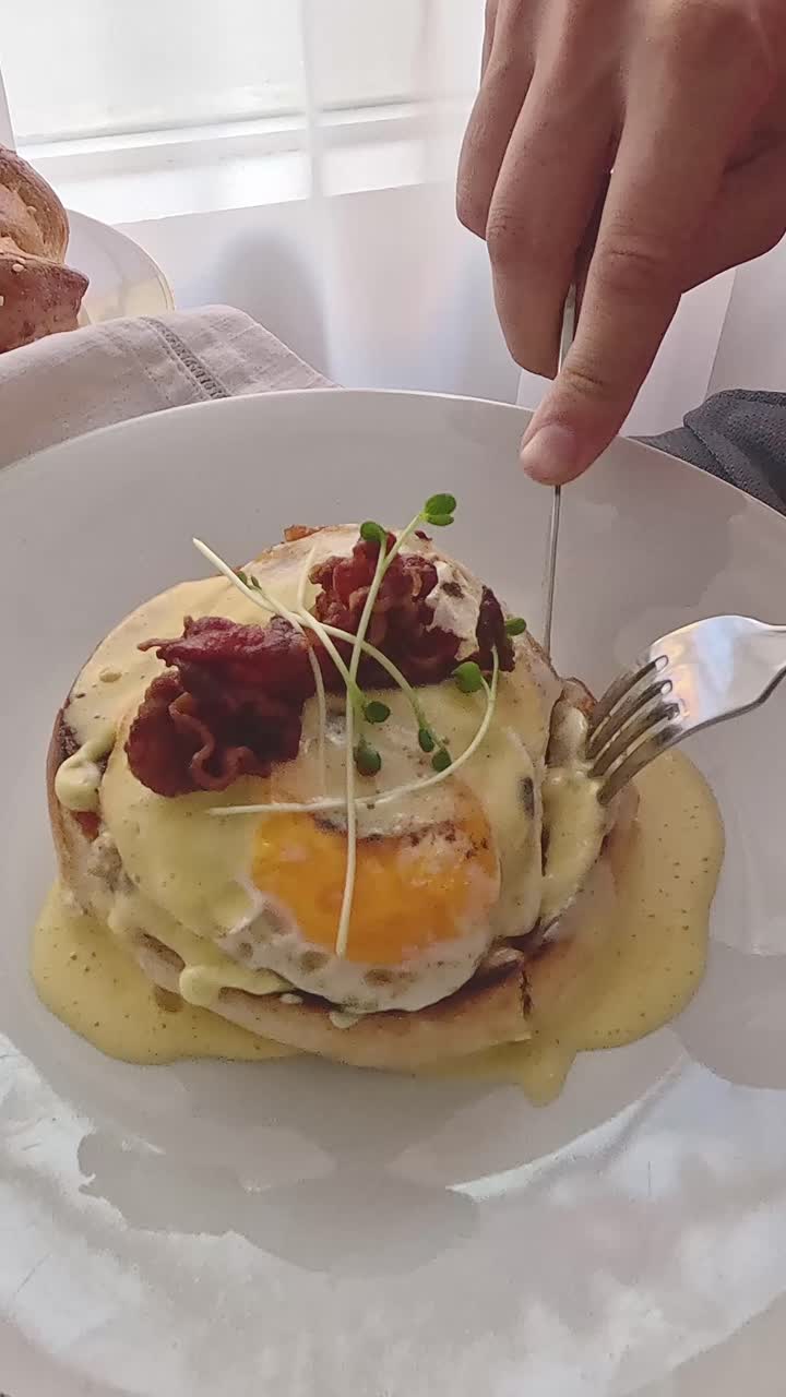 Using fork and knife to cut into croque monsieur, a classic french breakfast dish with eggs, ham and bechamel toppings