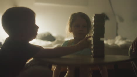 little boy makes move in board game by carefully pulling out wooden block. children play funny game carefully building tower. family relaxation