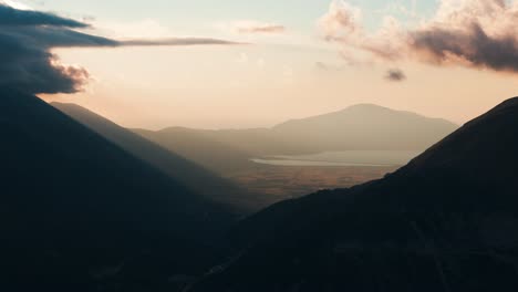 aerial view of dark and moody mountain valley, sun illuminate in background