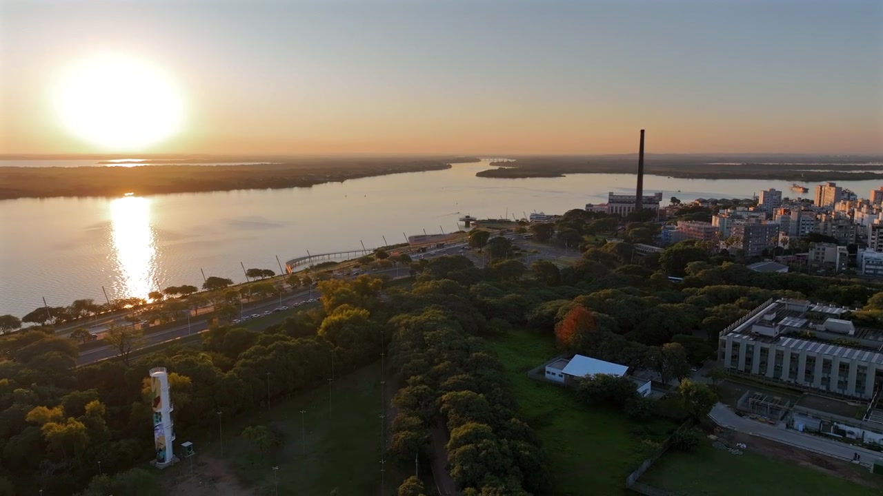 Parco lungofiume di Porto Alegre all'ora d'oro con l'acqua illuminata dal sole e l'iconica ciminiera del Gasometro in lontananza