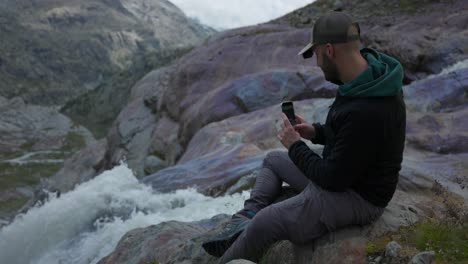 turista masculino toma fotos con su teléfono inteligente en una cascada de montaña