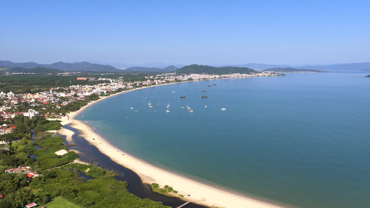 Praia da Cachoeira do Bom Jesus di Florianópolis Santa Catarina Brasil di Samudra Atlantik dengan teluk tenang, garis pantai berpasir, dan pegunungan Serra do Mar di latar belakang, penurunan drone