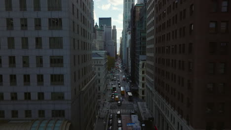 Backwards-reveal-of-one-way-street-between-tall-city-buildings.--Construction-site-aside-road.-Manhattan,-New-York-City,-USA