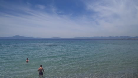 Left-pan-,-wide-footage-of-two-caucasian-boys-enjoying-the-beach-at-Kalamata,-Peloponnese,-Greece