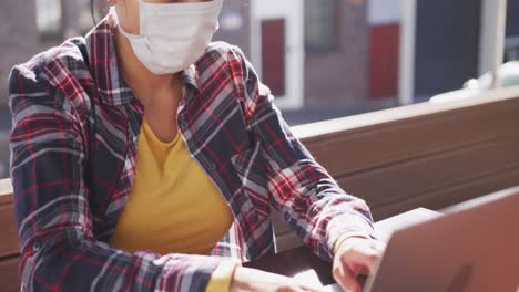 mixed race woman working on laptop wearing coronavirus mask