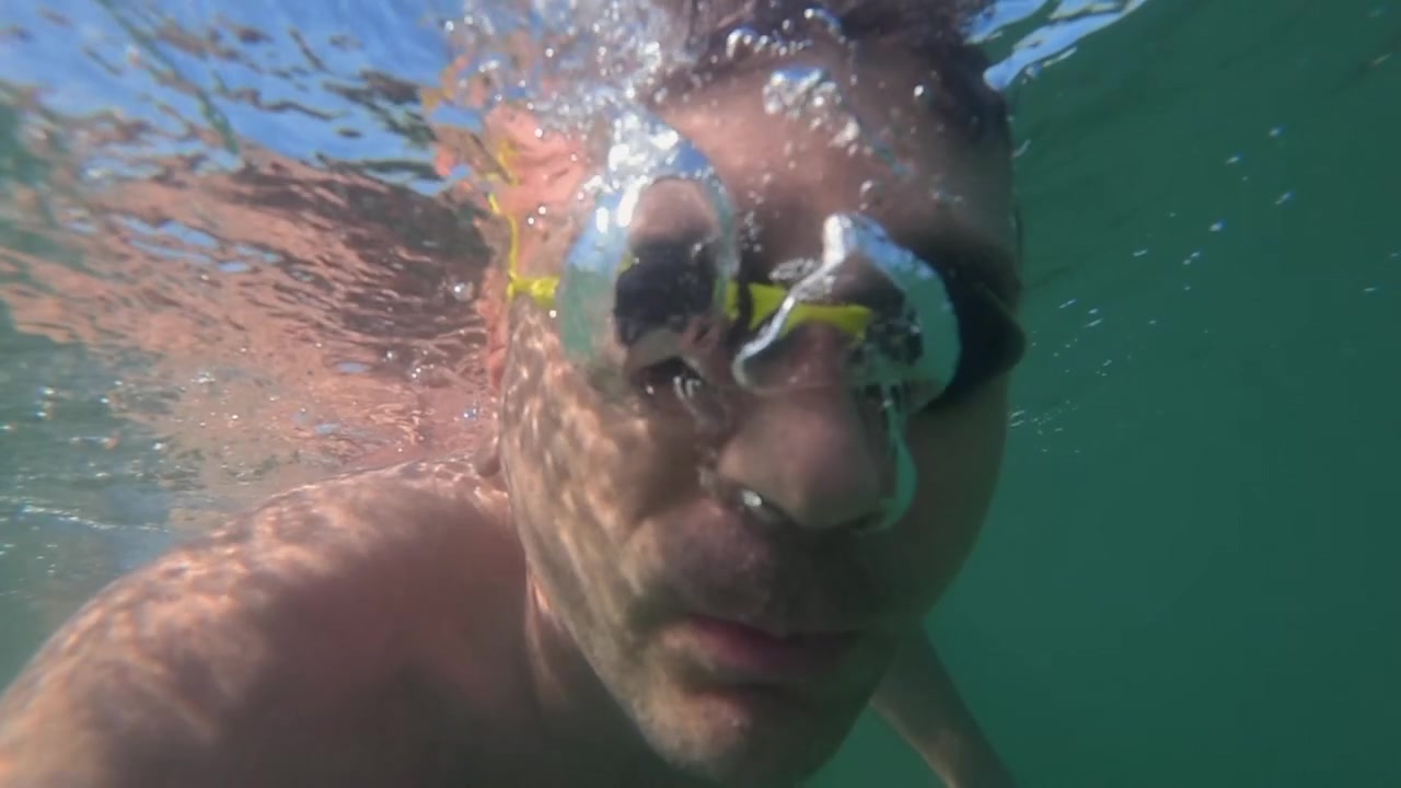 Uomo con occhialini da nuoto che si immerge sott'acqua, espirando bolle, godendosi l'attività estiva e la libertà nell'oceano.
