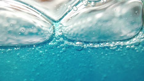 macro view of soap bubbles within blue liquid moving and growing