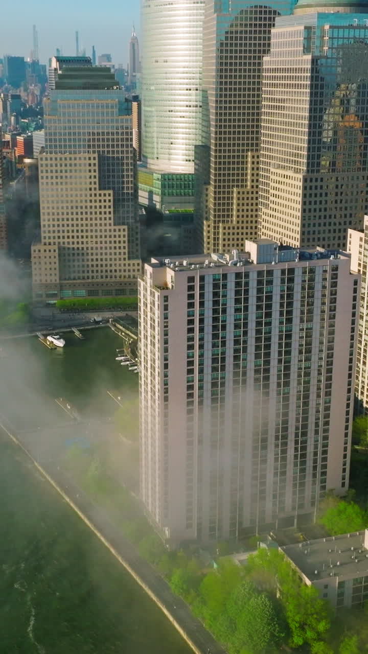 Manhattan Island skyscrapers reflecting morning sun. Flying over the East river waterfront covered with light smoke fog. Vertical video