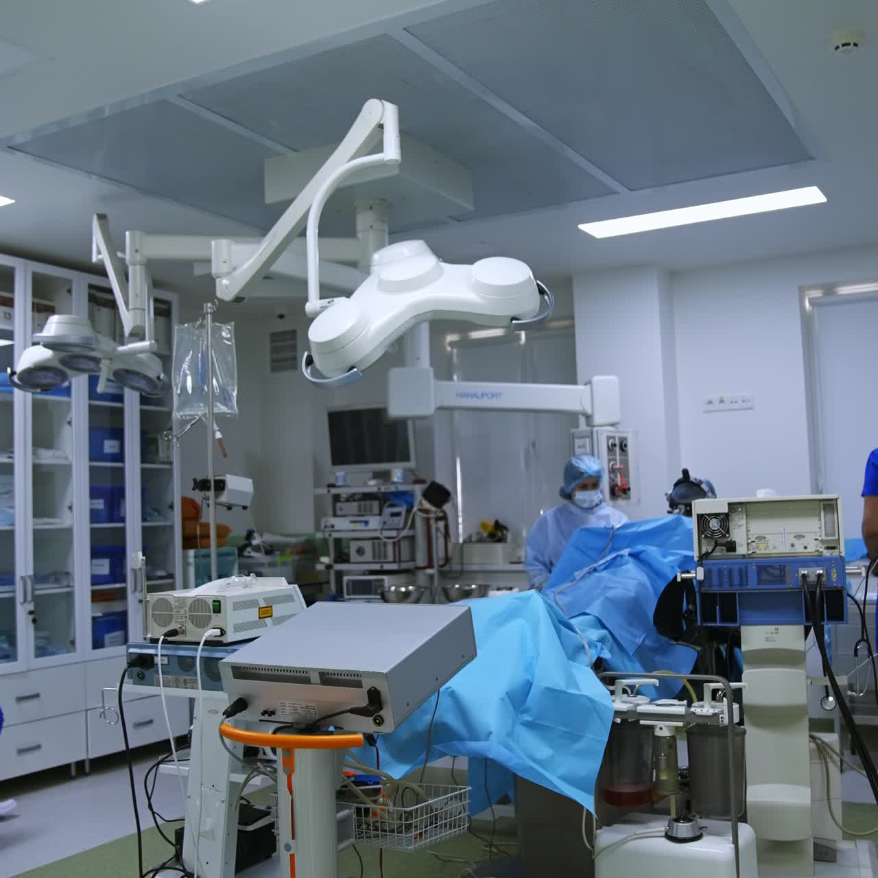 Vertical Screen: Slightly opened door to a well equipped modern operational theatre. Medics working at surgery inside the room