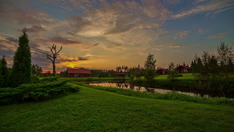 Tiro-De-Hiperlapso-De-Hermosa-Puesta-De-Sol-Sobre-El-Parque-Con-Lago-Y-Cabaña-En-El-Fondo---Lapso-De-Tiempo