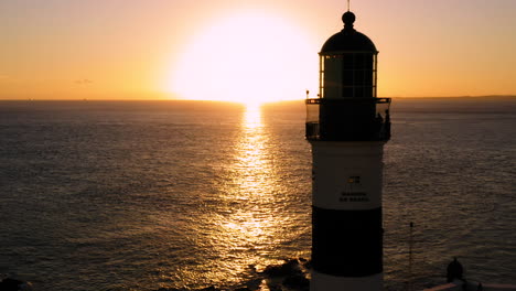 Aerial-view-of-Farol-da-Barra-illuminated-by-the-sun-and-the-sea,-at-sunset,-Salvador,-Bahia,-Brazil