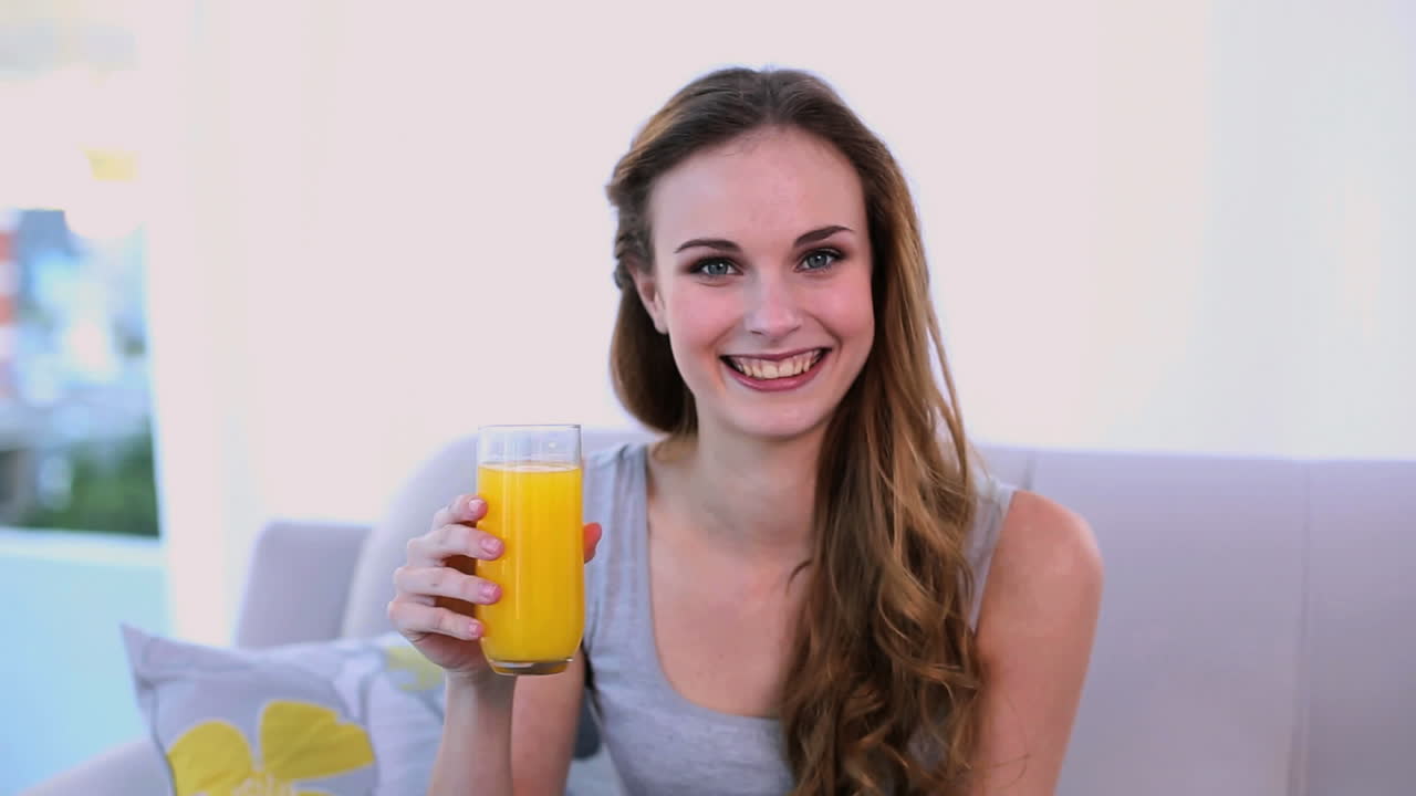 Modelo feliz bebiendo zumo de naranja en el sofá