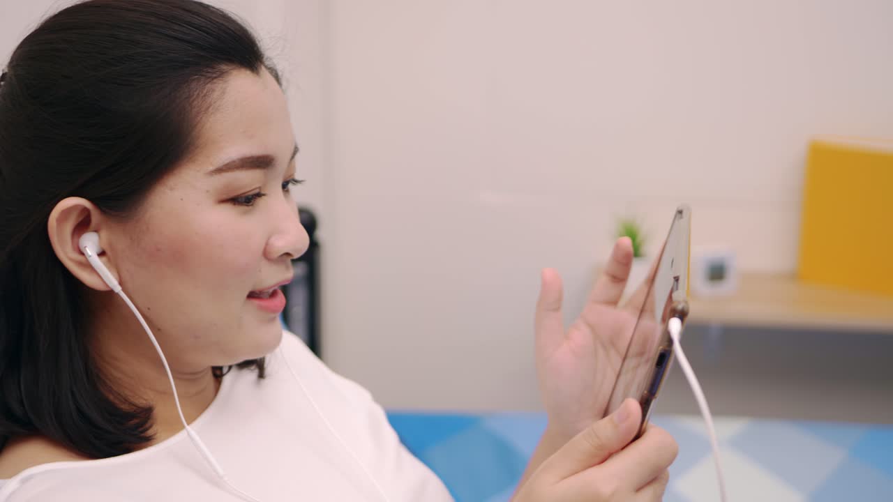 Cheerful young beautiful Asian woman relaxing and listening to music by tablet with headphones on the bed at home lifestyle and pleasure concept