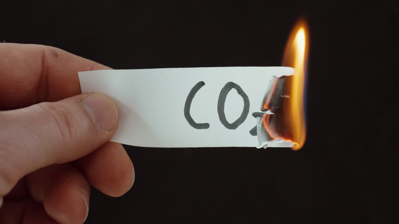 「CO2」と書かれた紙を燃やす手。炭素排出量、気候変動、環境への影響を象徴しています。
