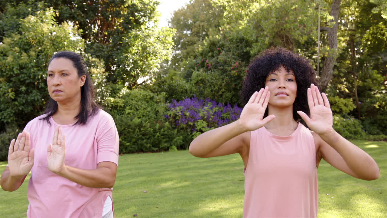 Practicing tai chi, mother and adult daughter exercising outdoors in park, enjoying fresh air