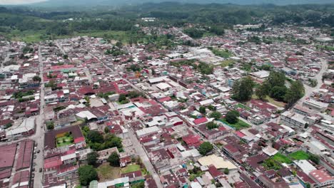 aerial zoom in over the city of cobán, guatemala, showing red rooftops and urban layout surrounded by green hills on a cloudy day