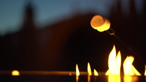 Appetizing-white-marshmallow-warming-up-over-gas-fire-pit-during-cozy-nightfall