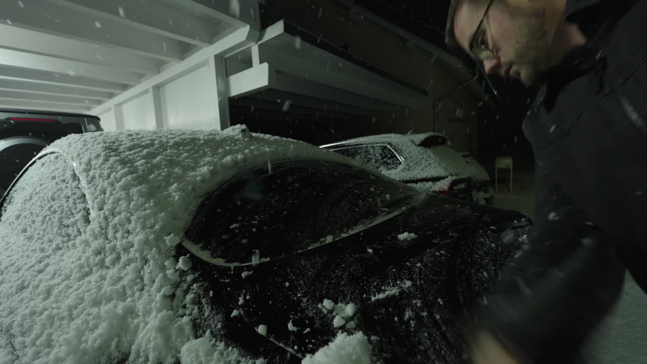 Una persona rimuove la neve da un'auto usando la manica in un parcheggio. Concetto di routine invernale, rimozione improvvisata della neve, sfide dovute al freddo e preparazione alla mobilità quotidiana