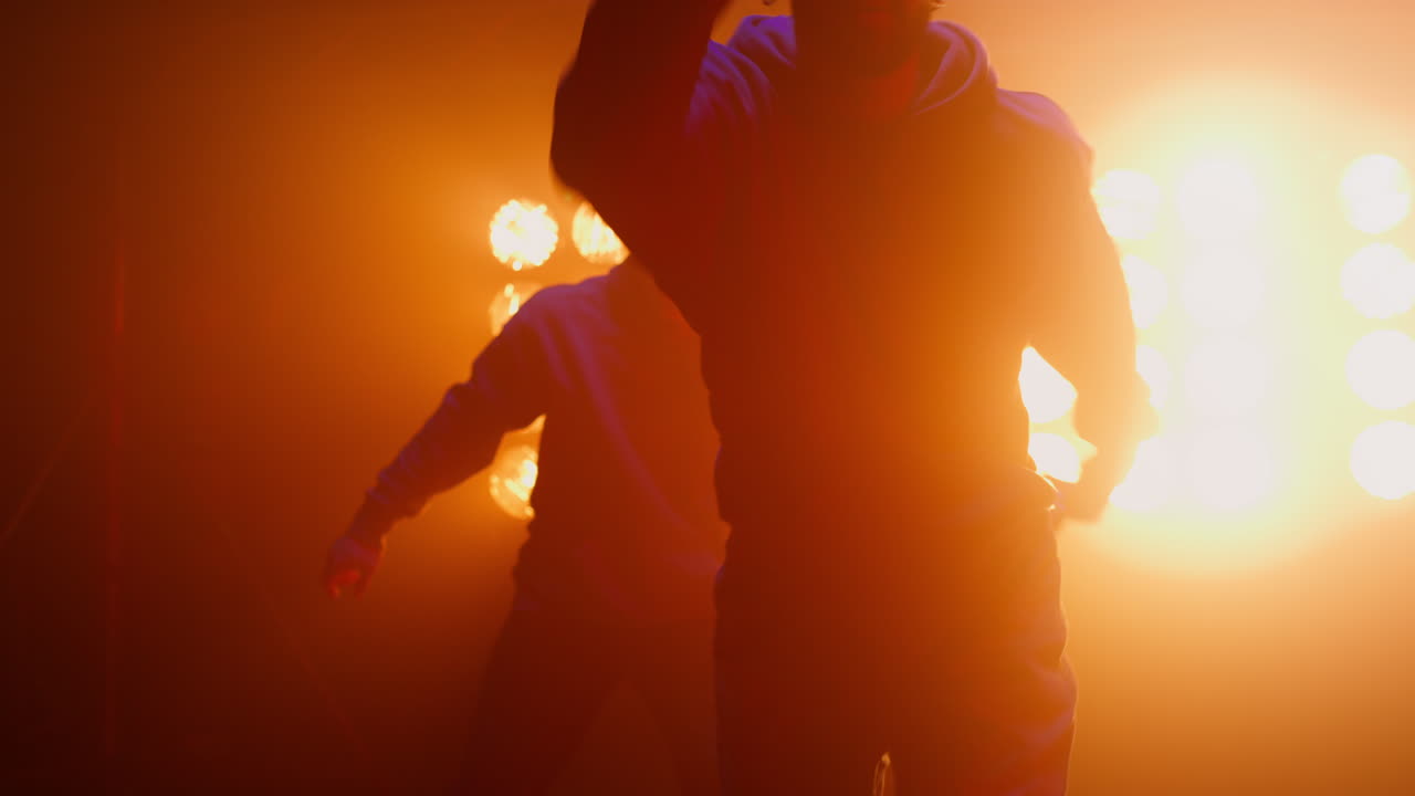 Jumping dancers performing hiphop on spotlight close up. Agile men team dancing.