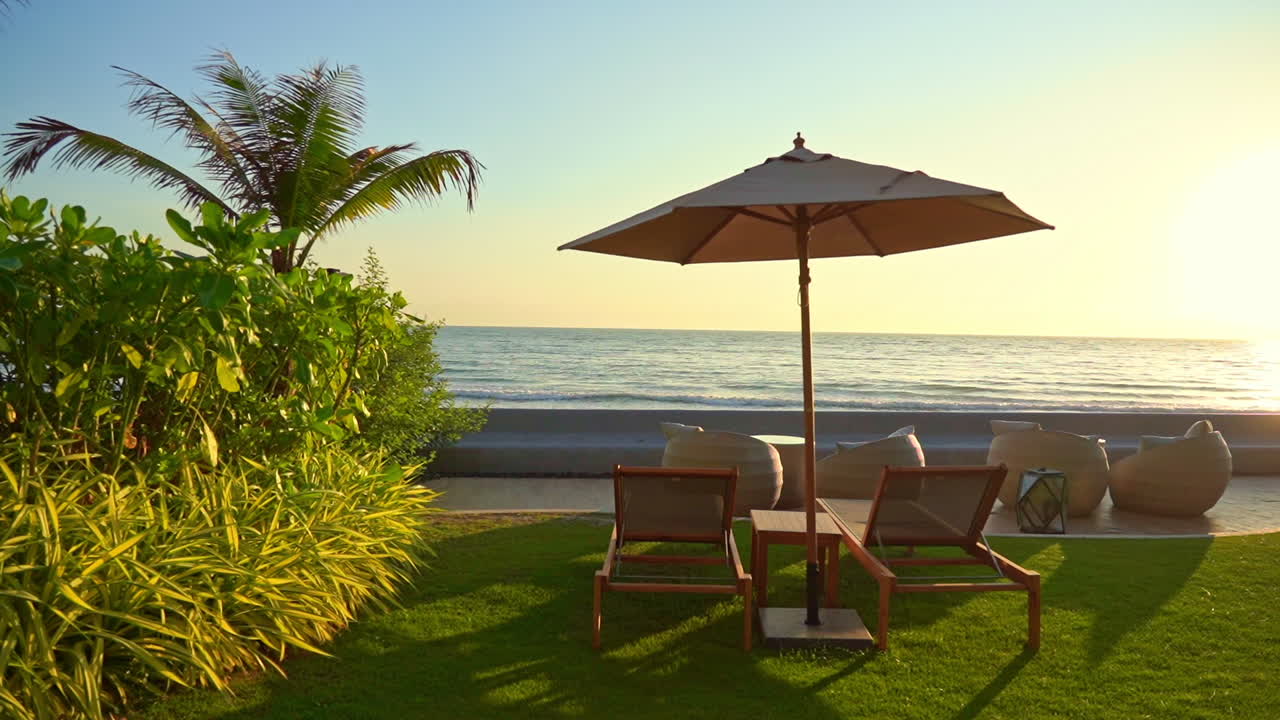 Lettini prendisole, ombrellone in lussureggiante giardino tropicale, vista sul mare durante l'alba