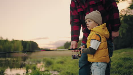 cute little boy is learning to fish granddad is helping him and teaching grandfather and grandchild