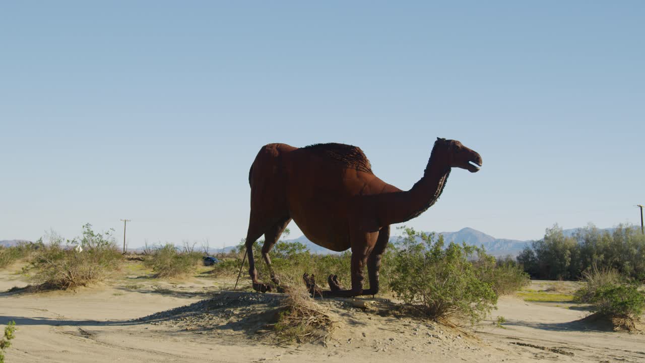 una estatua gigante de camello sentada en la tierra rodeada de pastizales de hierba y paisajes montañosos