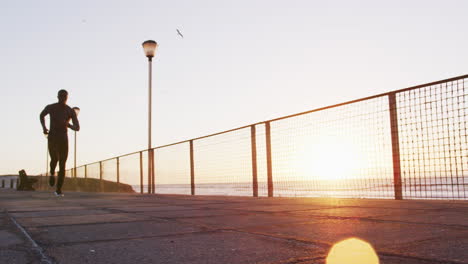 focused african american man running exercising outdoors by seaside at sunset