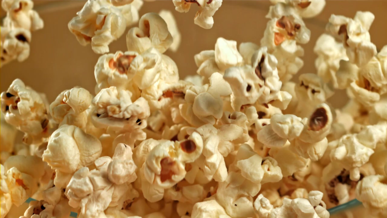 Palomitas de maíz frescas cayendo en un tazón de cristal en cámara lenta.
