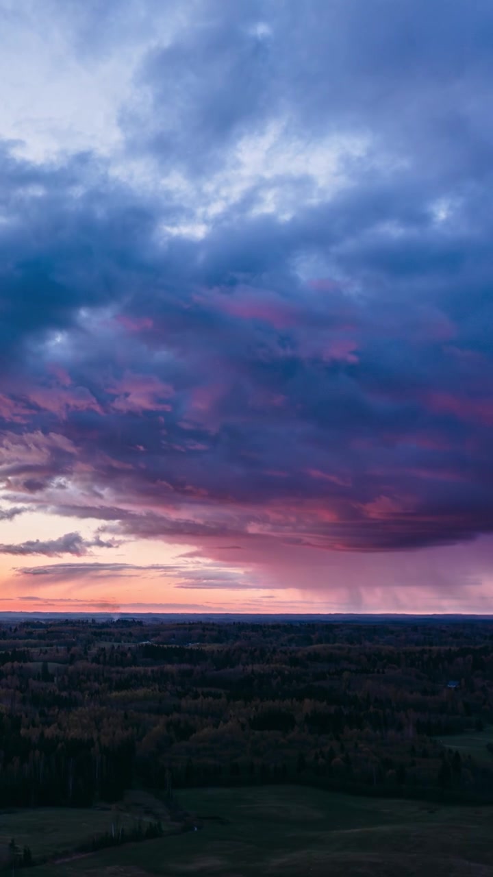 Cinematic vertical drone hyperlapse over a dark green forest landscape under a dramatic colorful storm sky at sunset golden hour.