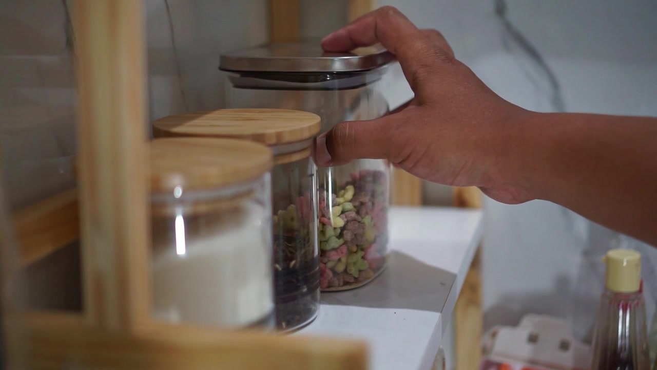 Persona che prende un barattolo di vetro pieno di cereali colorati dallo scaffale della dispensa, concetto di conservazione e organizzazione della cucina