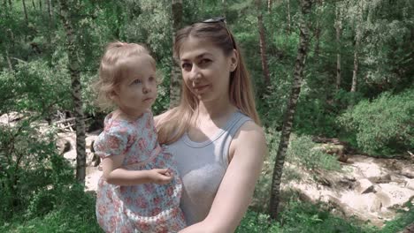 retrato de una hermosa madre joven con su hija en el bosque con un fondo de un río de montaña de primer plano en cámara lenta