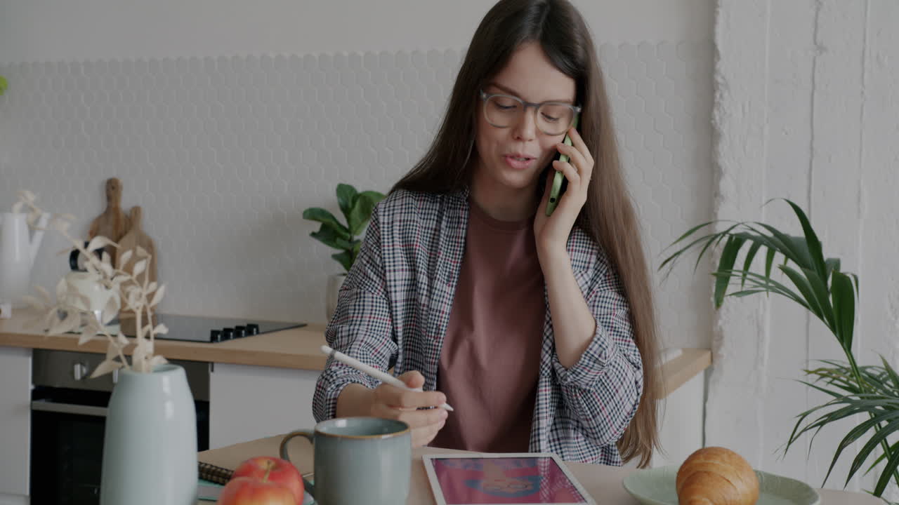Young Woman Working and Talking on Phone in Kitchen