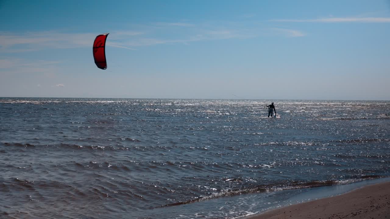 un surfista de cometas caminando en aguas poco profundas en su camino hacia el océano en un caluroso día de verano