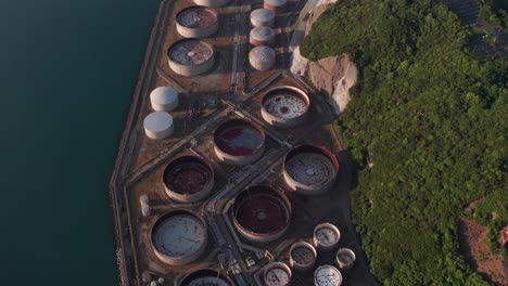 Aerial-drone-tops-down-refinery-oil-landscape-in-japanese-ocean-coastline-forest-in-hills,-petrol-tanks-slow-motion-establishing-shot-at-Japan-Wakayama