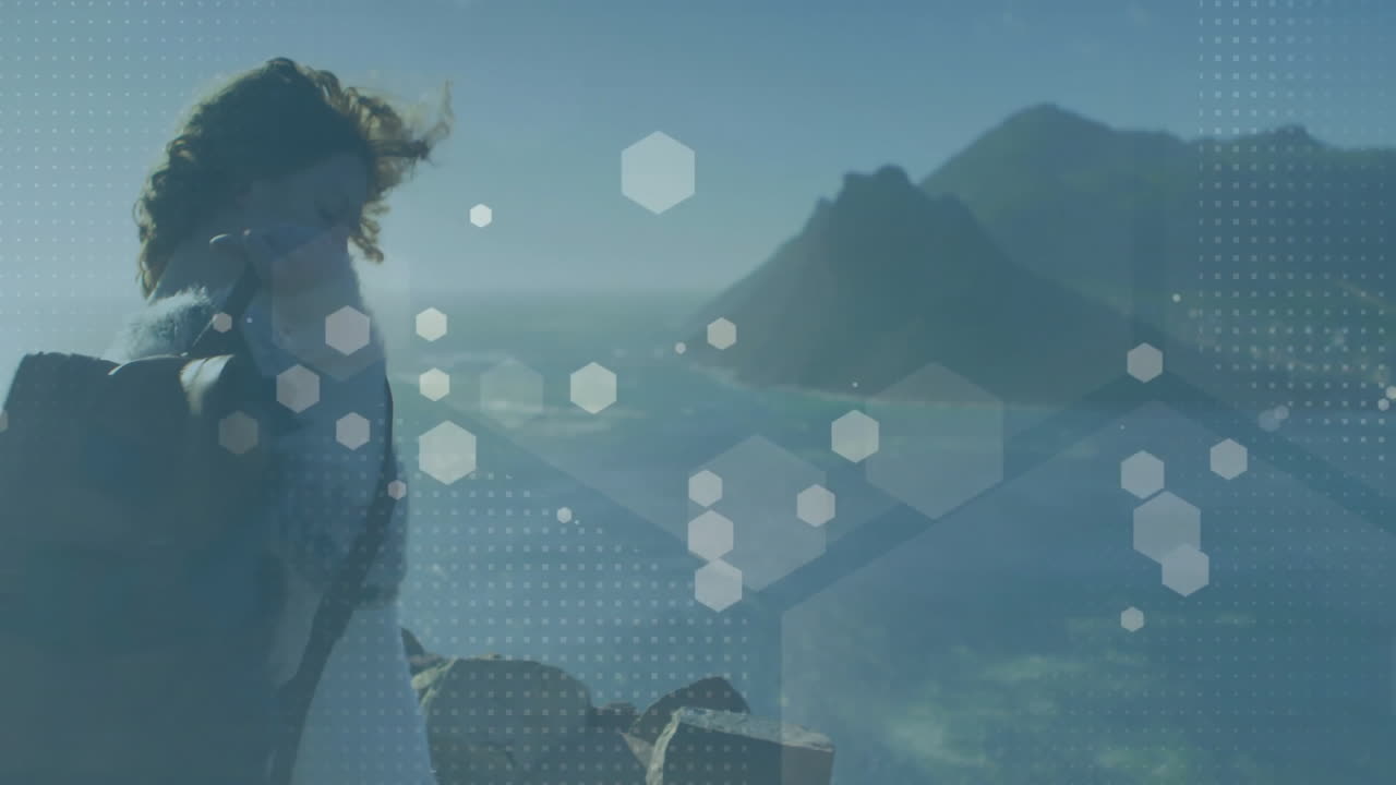 Woman standing on cliff overlooking lake and mountains, using hexagon graphics in travel technology