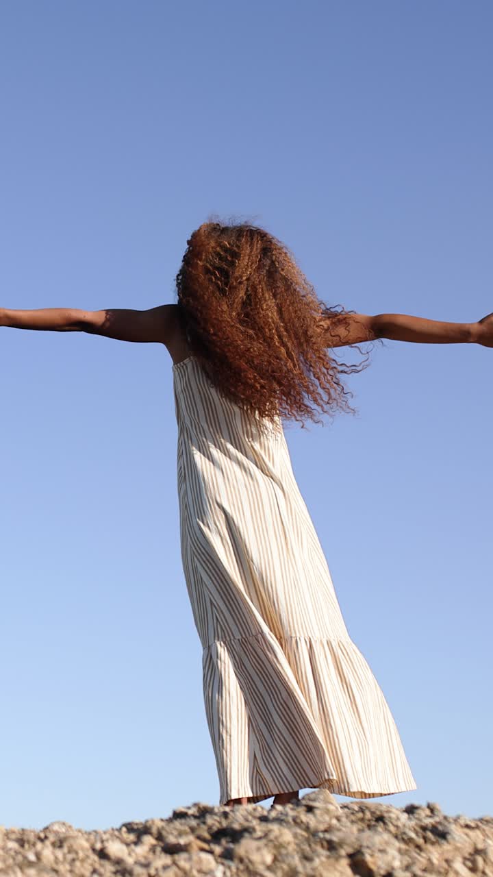 Woman with flowing hair and outstretched arms under a clear blue sky