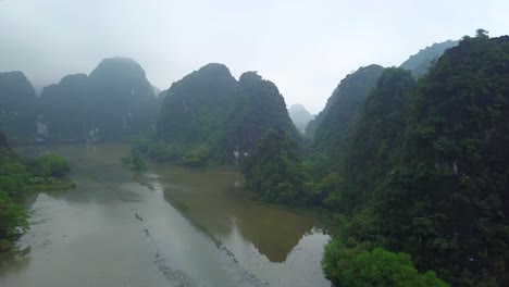 cinematic drone footage of majestic limestone peaks in misty and foggy weather. ricefields in wild jungle in the spring with boat tour canal in tam coc, ninh binh, vietnam