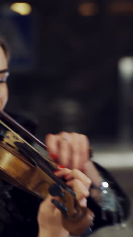 a charming girl is playing the violin in a black coat in the evening in the street. camera motion around vertical video